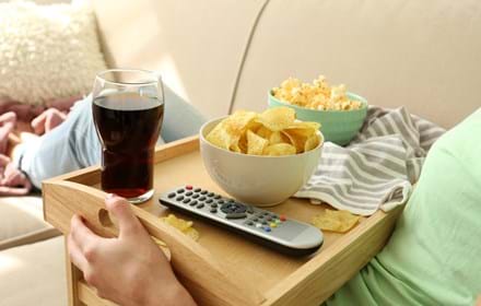 Person With Tray Of Chips And Drink On The Sofa