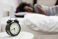 A person sleeping near an alarm clock. 